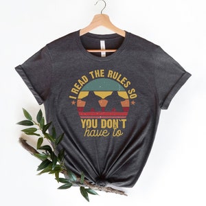 May include: Dark gray t-shirt with a vintage-style graphic that says "I read the rules so you don't have to".