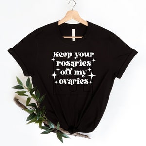May include: Black t-shirt with white text that reads "Keep your rosaries off my ovaries".