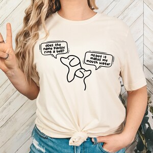 May include: A white t-shirt with a black illustration of two dogs. The text on the shirt says "does the name pavlov ring a bell?" and "no but it makes my mouth water."