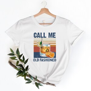 May include: White t-shirt with a vintage-style graphic of a glass of old fashioned with the text "Call Me Old Fashioned".