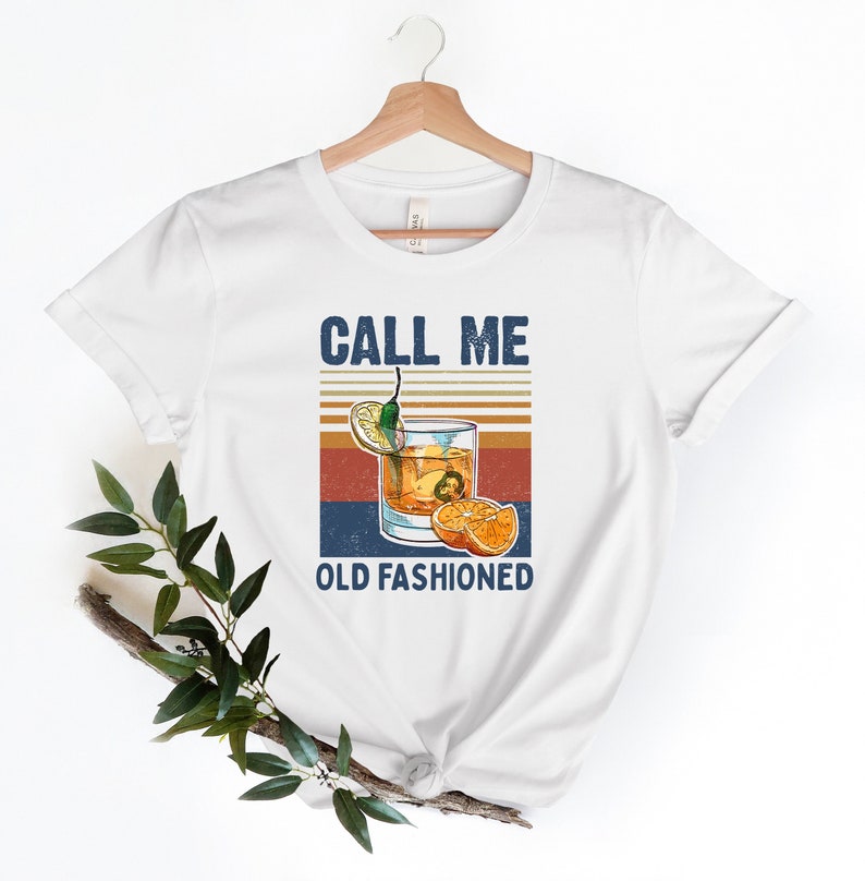 May include: White t-shirt with a vintage-style graphic of a glass of old fashioned with the text "Call Me Old Fashioned".