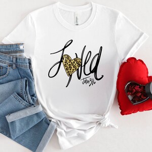 May include: White t-shirt with a black and gold leopard print heart and the text "Loved" with "John 3:16" underneath.