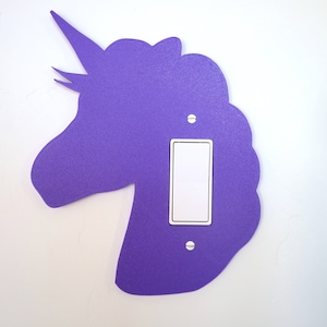 May include: Purple unicorn light switch cover. The unicorn is a silhouette with a horn and mane. The light switch is white and is in the center of the unicorn's head.