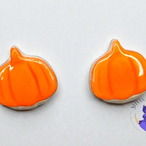 May include: Two orange pumpkin-shaped ornaments with a glossy finish. Each pumpkin has vertical grooves and a small stem. The ornaments are set against a white background. The logo of "Sylvan Baubles" is in the bottom right corner.