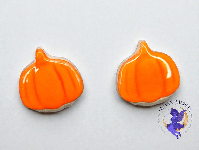 Peut inclure: Deux ornements en forme de citrouille orange avec une finition brillante. Chaque citrouille pr&eacute;sente des rainures verticales et une petite tige. Les ornements sont pos&eacute;s sur un fond blanc. Le logo "Sylvan Baubles" est dans le coin inf&eacute;rieur droit.