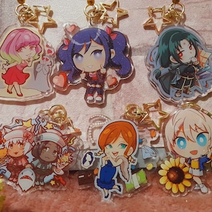 May include: Six colorful acrylic keychains featuring anime-style characters. Each keychain has a gold chain and a star-shaped charm. The characters include a girl with pink hair, a girl with blue hair, a boy with green hair, a girl with white hair, a girl with brown hair, and a girl with black hair.