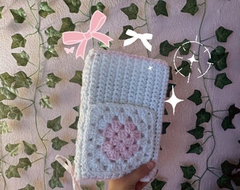 May include: A white crocheted pouch with a pink crocheted square pocket. The pouch has a white ribbon attached to it.