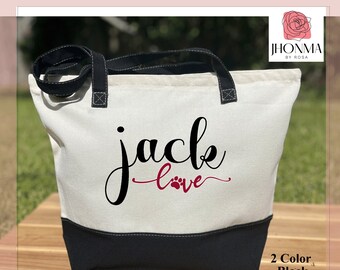 May include: A white canvas tote bag with black handles and a black base. The bag features the text "jack love" in black with a red paw print. The bag is made in the USA.