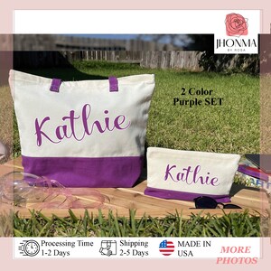 May include: A set of two personalized tote bags with the name "Kathie" embroidered on them. The larger tote bag is white with a purple bottom and the smaller tote bag is white with a purple top. Both bags are made of canvas.