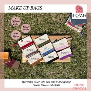 May include: Makeup bags in eight different colors, including maroon, grey, green, blue, pink, purple, black, and brown. Each bag has a zipper and is lined inside. The bags are displayed on a wooden surface.