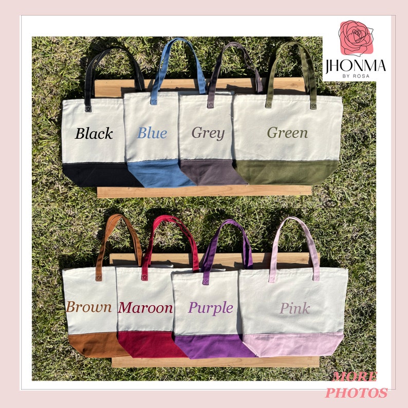 May include: Canvas tote bags in various colors: black, blue, grey, green, brown, maroon, purple, and pink. Each bag has a contrasting bottom panel and matching handles. The names of the colors are printed on the bags.
