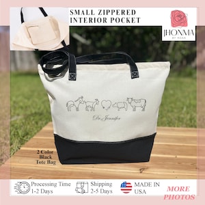 May include: A two-tone tote bag with a black base and a cream-colored upper section. The bag features black handles and a small zippered interior pocket. The bag is decorated with line drawings of farm animals and the text "Dr. Jennifer".