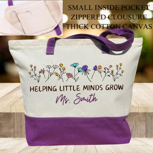 May include: A white canvas tote bag with purple handles and a purple bottom. The bag has a small inside pocket with a zippered closure. The bag has a floral design and the text "Helping Little Minds Grow Ms. Smith".
