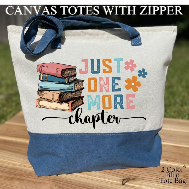May include: A canvas tote bag with a zipper, featuring a two-tone design. The top portion is off-white, while the bottom and handles are blue. The bag displays the text "JUST ONE MORE chapter" with a stack of books and floral accents.