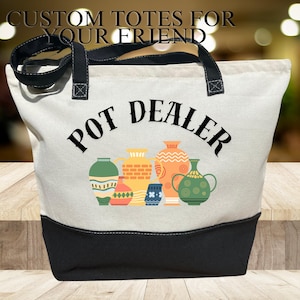 May include: A white canvas tote bag with black handles and a black bottom. The bag has a design of colorful pots and the text "Pot Dealer" in black.