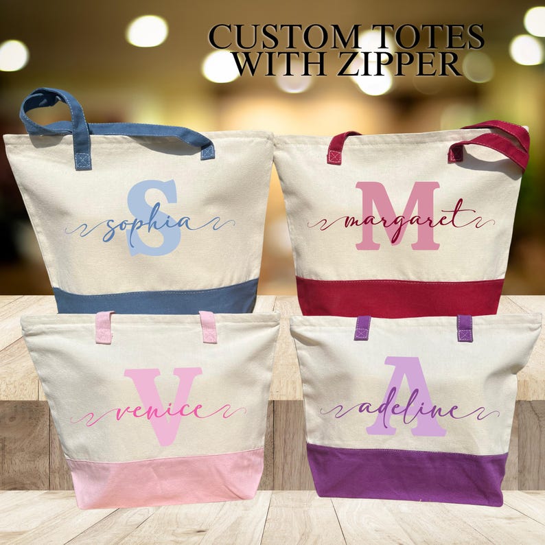 May include: Four custom tote bags with zipper closures. Each bag is made of natural canvas with a contrasting colored bottom. The bags are personalized with a large initial and a name in cursive script. The names are "Sophia", "Margaret", "Venice", and "Adeline".