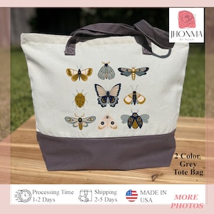 May include: A grey canvas tote bag with a design of various butterflies and moths in shades of blue, yellow, and white. The bag has a grey bottom and two grey handles.
