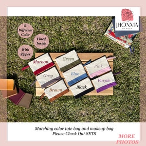 May include: Eight different color makeup bags with a zipper and lined inside. The bags are laid out on a wooden surface with a brown, grey, black, blue, green, maroon, pink, and purple color scheme. The bags are made of canvas with a contrasting color trim.
