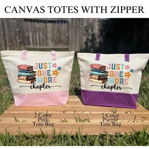 May include: Two canvas tote bags with zippers, one pink and one purple. Each bag has a cream-colored upper section and a colored bottom. The bags feature the text "JUST ONE MORE chapter" with a stack of books and floral accents.