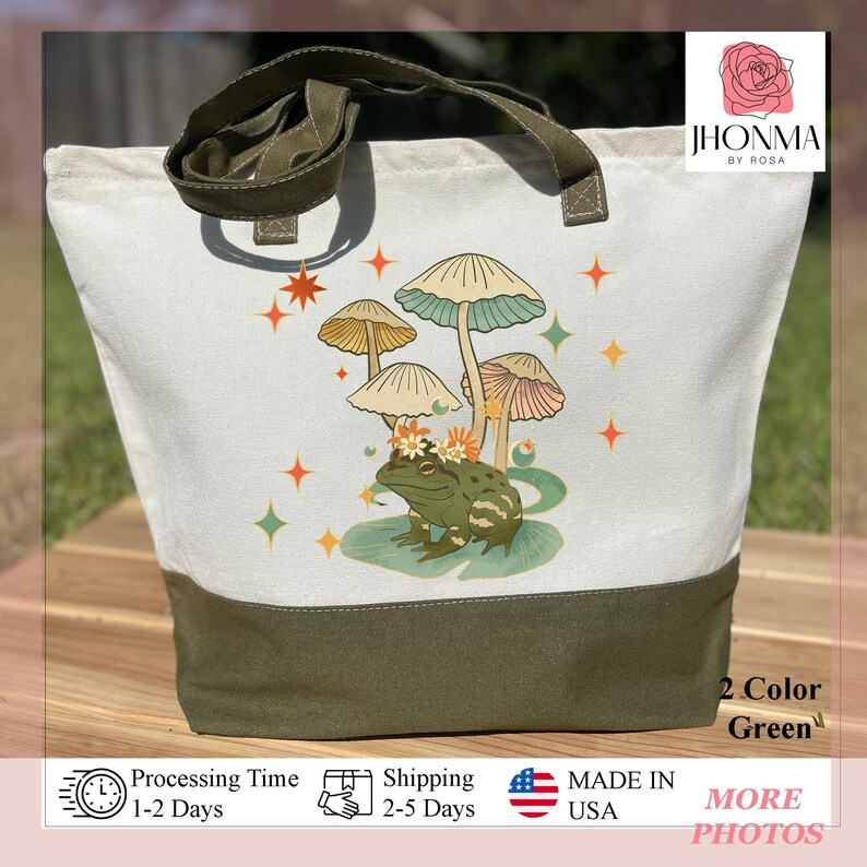 K&ouml;nnte beinhalten: Eine wei&szlig;e Canvas-Tragetasche mit gr&uuml;nem Boden. Die Tasche zeigt eine fantasievolle Illustration eines Frosches mit einer Blumenkrone, der auf einem Seerosenblatt sitzt, umgeben von Pilzen und Sternen. Der Text "JHONMA BY ROSA" ist in der oberen rechten Ecke der Tasche aufgedruckt.