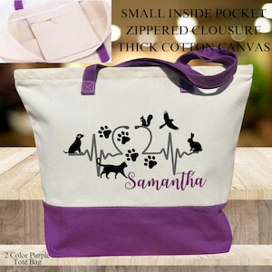 May include: A white canvas tote bag with purple handles and a purple bottom. The bag has a black design of a heart with a stethoscope, paw prints, and animals including a cat, dog, squirrel, bird, and rabbit. The text "Samantha" is printed below the design. The bag has a small inside pocket with a zippered closure. The bag is made of thick cotton canvas.