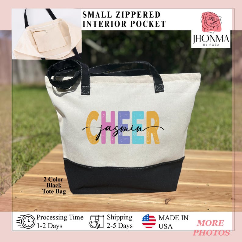 May include: A white canvas tote bag with black handles and a black bottom. The bag has a small zippered interior pocket. The front of the bag has the words "CHEER" in colorful letters with the name "jasmin" written in cursive underneath. The bag is sitting on a wooden surface.