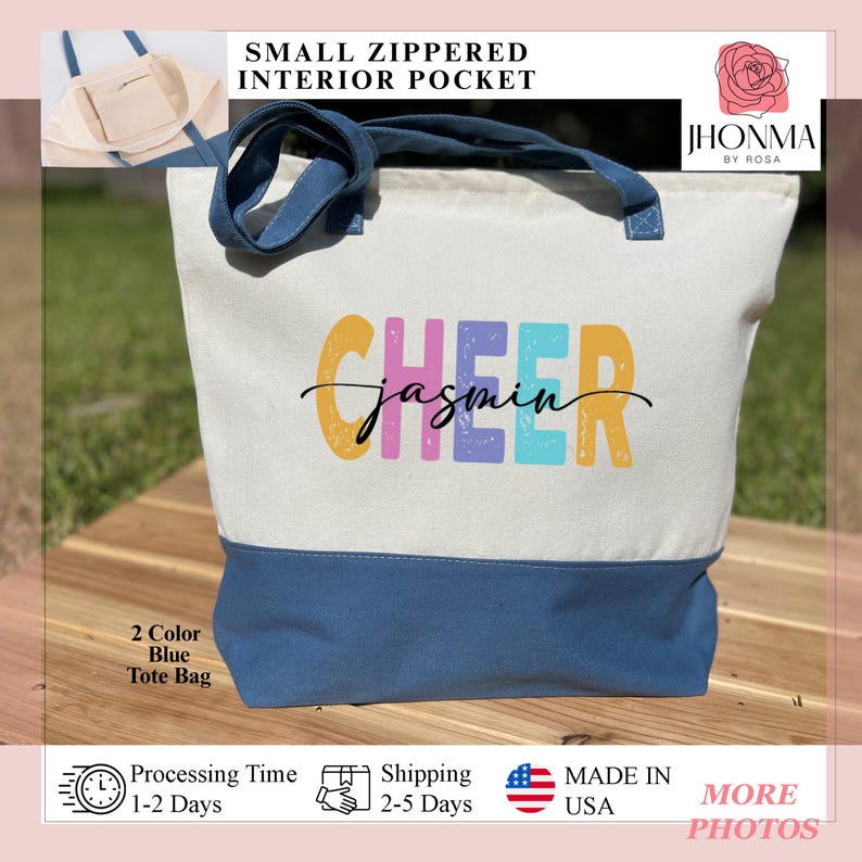May include: A white canvas tote bag with a blue bottom. The bag has a small zippered pocket on the inside. The bag has the text "CHEER" in colorful letters with the name "jasmin" written in cursive underneath. The bag is sitting on a wooden surface.