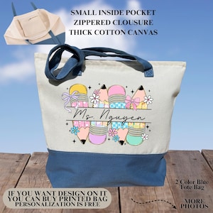 May include: A canvas tote bag with a blue base and handles, featuring a colorful pencil and eraser design. The bag includes the text "Ms. Nguyen" and additional text: "Small inside pocket, zippered closure, thick cotton canvas."