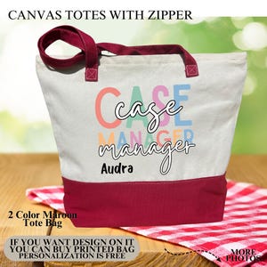 May include: A canvas tote bag with a zipper, featuring a white upper section and a maroon bottom. The bag has maroon handles and the words "Case Manager" in colorful letters. The name "Audra" is printed below the text. The bag is on a wooden surface.