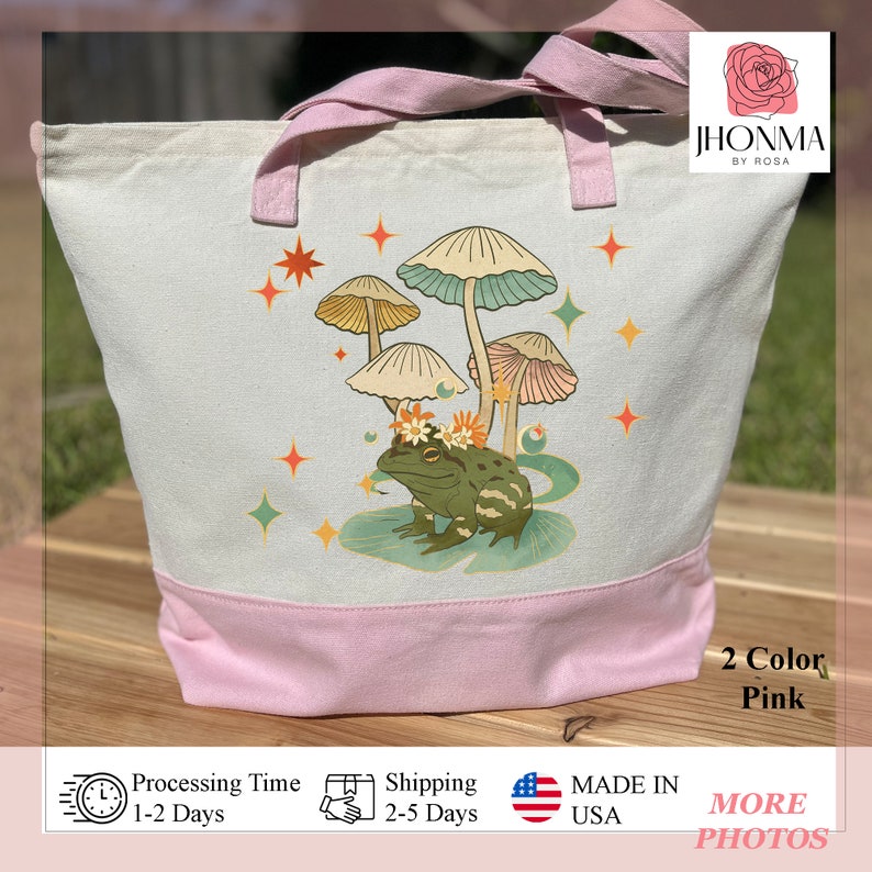 K&ouml;nnte beinhalten: Eine rosa-wei&szlig;e Canvas-Tragetasche mit einem verspielten Design, das einen Frosch mit einer Blumenkrone zeigt, umgeben von Pilzen und Sternen. Die Tasche tr&auml;gt den Text "JHONMA BY ROSA" und "2 Color Pink".