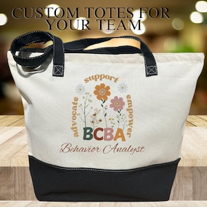 May include: A white canvas tote bag with black handles and a black bottom. The bag has a floral design with the words "support, advocate, empower" surrounding the letters "BCBA" and the words "Behavior Analyst".