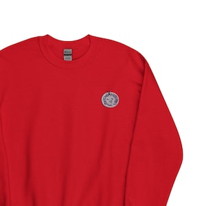 May include: A red long-sleeved sweatshirt with a small, round, blue and white logo on the left chest.