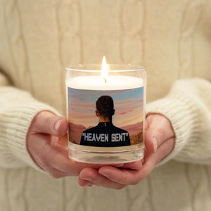 May include: A white candle with a clear glass jar and a photo of a person's back with the text "HEAVEN SENT" printed on the bottom of the photo.