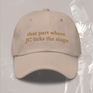 Op de afbeelding: Een beige baseballpet met de tekst "that part where JC licks the stage" geborduurd in bruin op de voorkant.