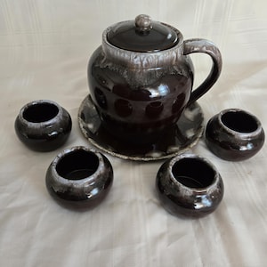 May include: A set of brown and white glazed ceramic serving dishes. The set includes a large pitcher with a lid and four smaller bowls. The dishes have a rustic, vintage look.