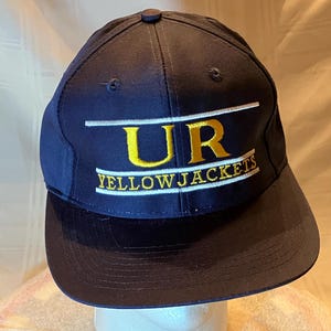May include: Navy blue baseball cap with a curved brim. The cap features the text "UR YELLOWJACKETS" in yellow and white embroidery. The cap has a button on top and is likely made of a durable fabric.