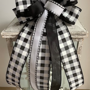 May include: Black and white buffalo plaid ribbon bow with a white satin ribbon, tied around a white lantern.