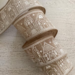 Peut inclure: Un rouleau de ruban en toile de jute beige avec un motif répété de maisons en pain d'épices blanches. Le ruban a un aspect texturé. Les maisons présentent des fenêtres, des portes et des éléments décoratifs détaillés. Le ruban est enroulé, montrant le motif.