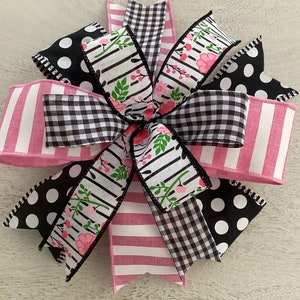 Könnte beinhalten: Eine rosa und schwarze Schleife mit Blumenmuster, Gingham und Punkten. Die Schleife ist aus Band und hat einen drahtverstärkten Rand.