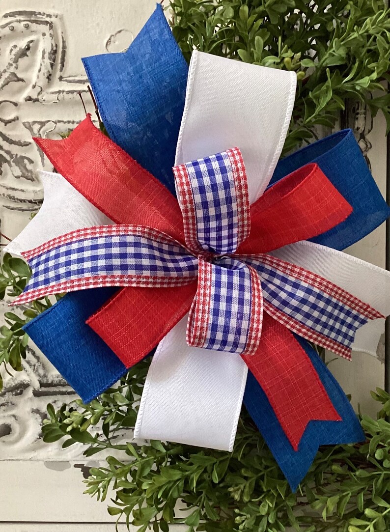 May include: A red, white, and blue bow made with gingham and burlap ribbon. The bow is tied around a wreath of green boxwood.