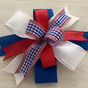 May include: A red, white, and blue bow made with ribbon. The bow is tied with a checkered ribbon in the center.