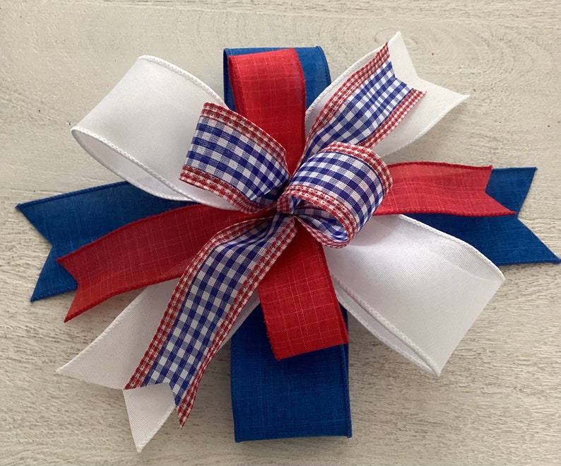 May include: A red, white, and blue bow made with ribbon. The bow is tied with a checkered ribbon in the center.