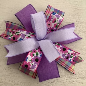 Könnte beinhalten: Eine violette und rosafarbene Blumen Schleife mit einem karierten Band. Die Schleife besteht aus mehreren Schichten Band und ist in der Mitte verknotet.
