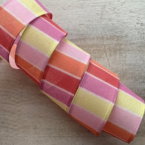 May include: A roll of striped ribbon in shades of pink, yellow, and orange. The ribbon is folded in a spiral shape.