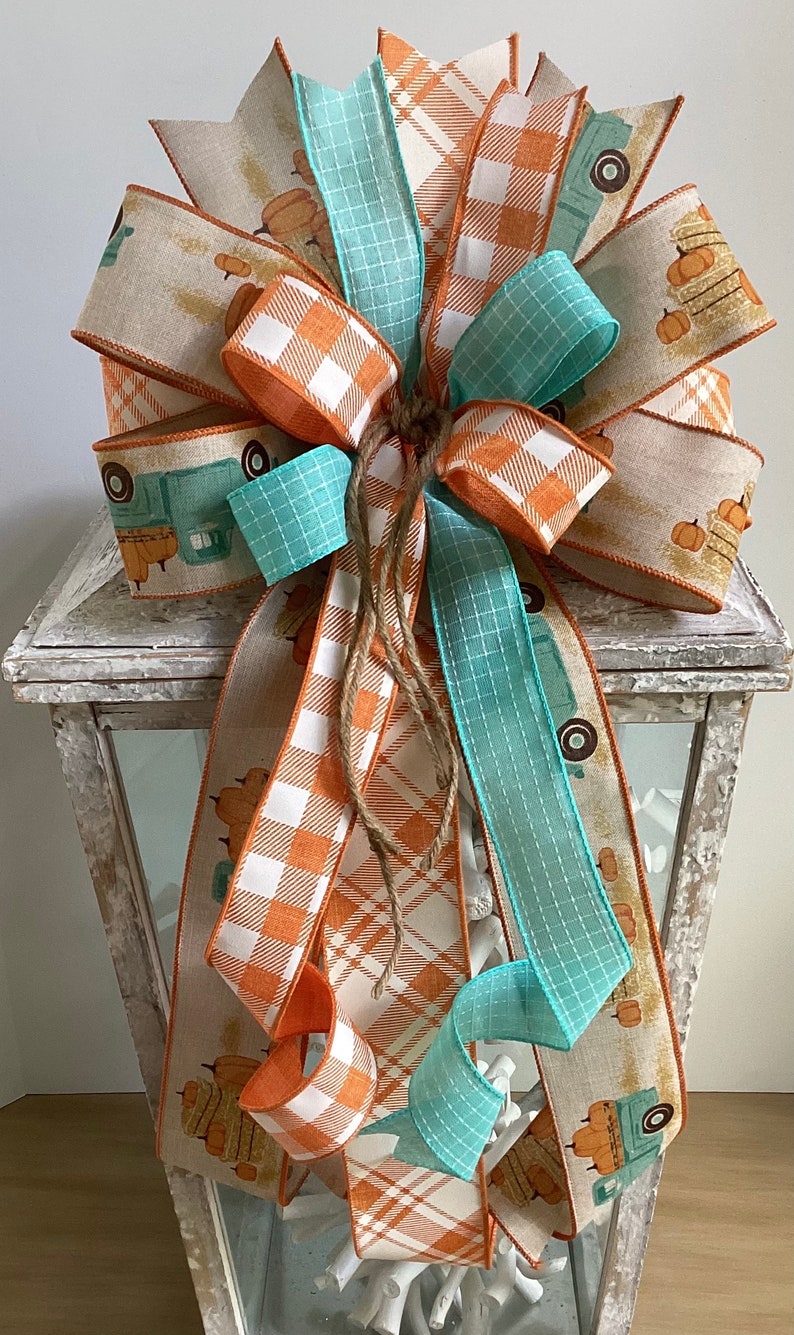 May include: A fall-themed lantern decoration with a large bow made of orange and white plaid ribbon, teal ribbon, and burlap ribbon with a vintage truck and pumpkin print.