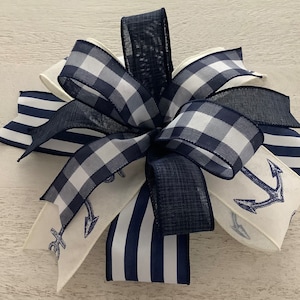 Könnte beinhalten: Eine Schleife aus marineblauem und weißem kariertem Band mit einem marineblauen Band und einem weißen Band mit einem marineblauen Ankerdruck. Die Schleife ist mit einem marineblauen Band zusammengebunden.