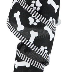 May include: A roll of black ribbon featuring white dog bone and paw print designs. The ribbon has a striped border and is suitable for crafting or gift wrapping. The ribbon is on a white spool.