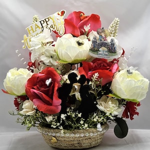 La composition florale Joyeux anniversaire comprend un couple qui s'embrasse, un signe sentimental, un même cœur que nous partageons, des cœurs brillants/une bordure en perles