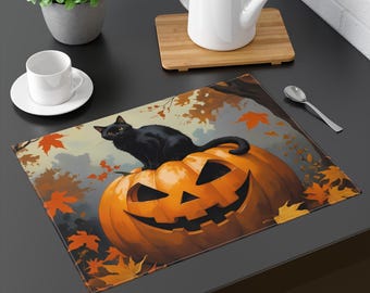 May include: A rectangular placemat with a black cat sitting on a carved orange pumpkin. The pumpkin has a smiling face. Autumn leaves and a tree branch are in the background. The placemat is on a black surface.