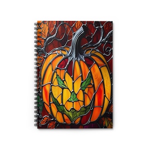 May include: Spiral-bound notebook featuring a stained-glass style pumpkin design. The pumpkin is orange and yellow with a green face, set against a red and brown background. The design evokes a Halloween theme.